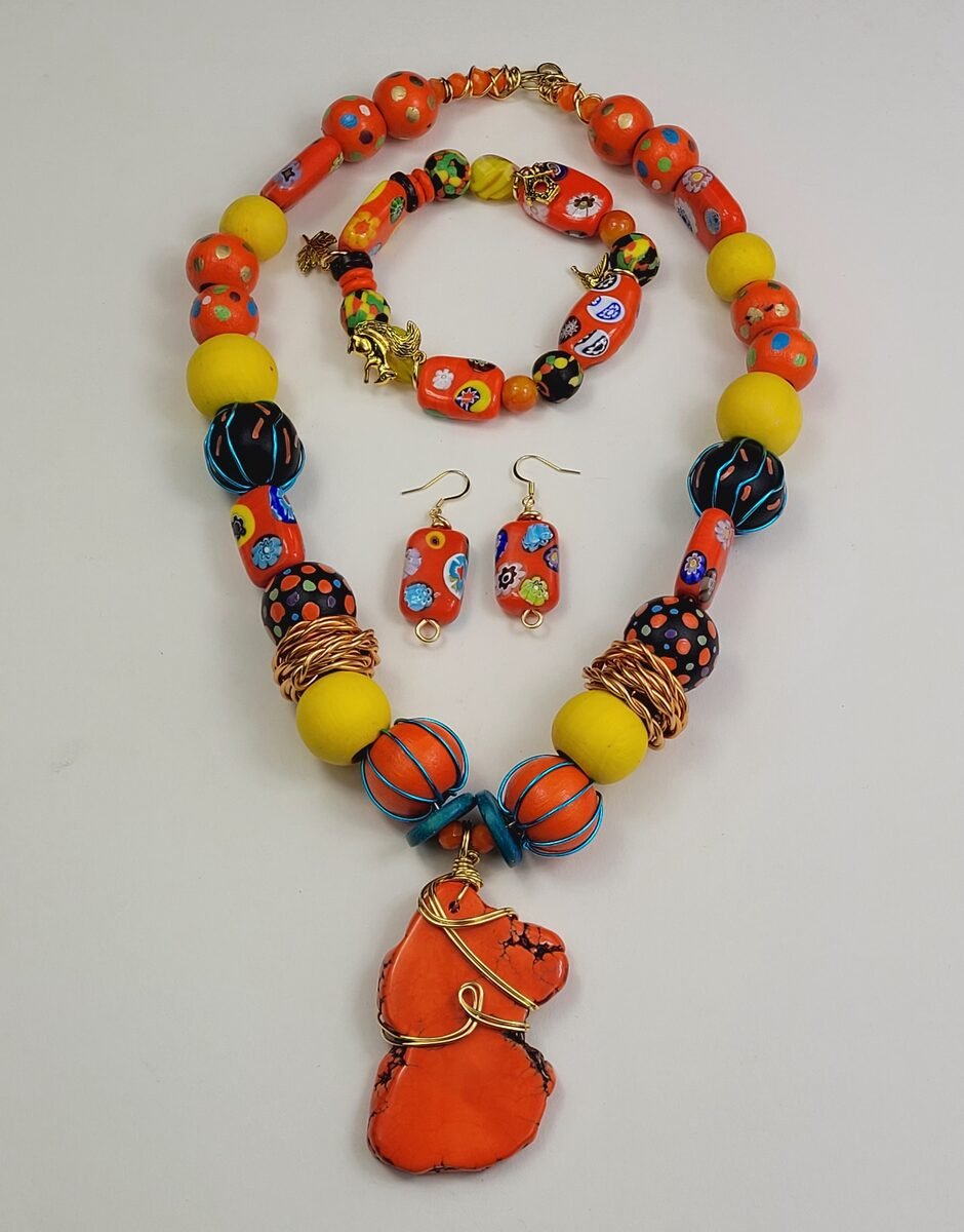 Vibrant orange beaded necklace with hand-painted millefiori beads and a wire-wrapped orange pendant, matching bracelet and earrings.