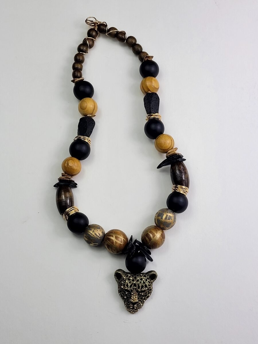 Warm-toned necklace mixing matte black, wood, and carved tiger-pattern beads with a bold gold leopard head pendant.